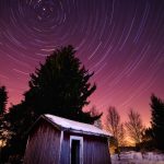 A Barn In The Snow With Star Trails In The Sky