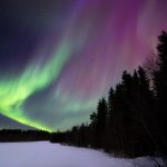 A Purple And Green Aurora Over A Snow Covered Field