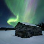Majestic Aurora Borealis Over A Rustic Cabin In A Snowy Winter Landscape At Night