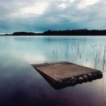 Serene Lakeside View With Concrete Pier And Reeds At Dusk