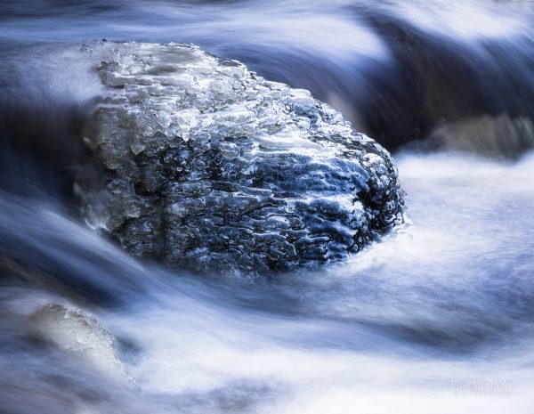 Serene Winter Stream Flowing Over A Partially Ice-Covered Rock