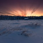 Winter Sunrise Over A Snow-Covered Landscape With Distant Forest And Cabin